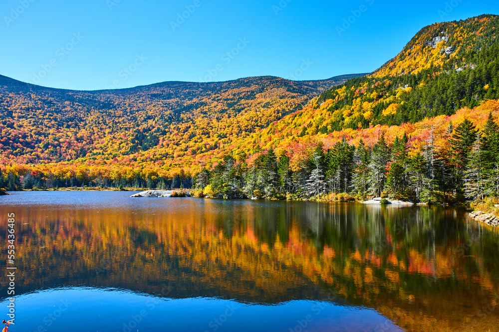 Beautiful lake reflecting mountains of fall foliage in New Hampshire