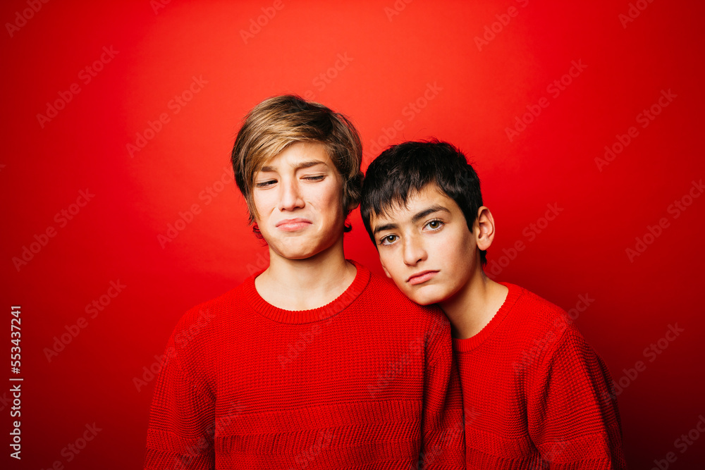 Studio portrait of two pre-adolescent boys, wearing a red sweater, embracing over a red background Studio portrait of two pre-adolescent boys, wearing a red sweater, embracing over a red background