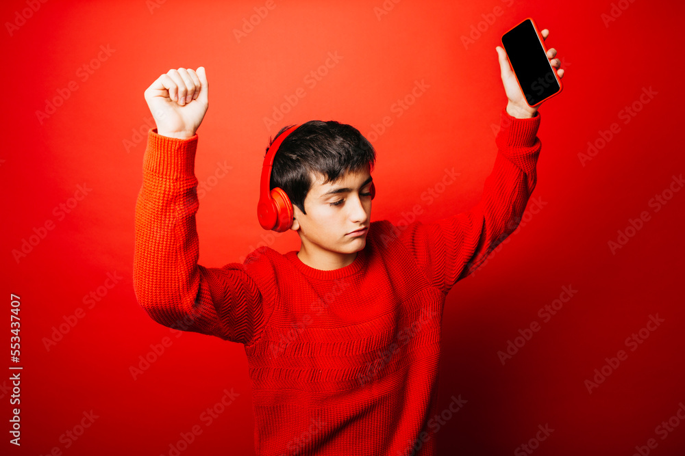 Studio portrait of a pre-adolescent boy, wearing a red sweater and red headphones over a red background, listening music and dancing Studio portrait of a pre-adolescent boy, wearing a red sweater and red headphones over a red background, listening music and dancing