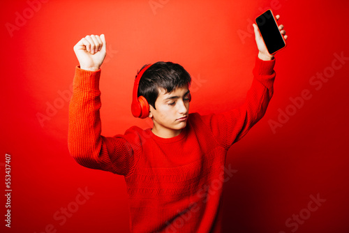 Studio portrait of a pre-adolescent boy, wearing a red sweater and red headphones over a red background, listening music and dancing photo