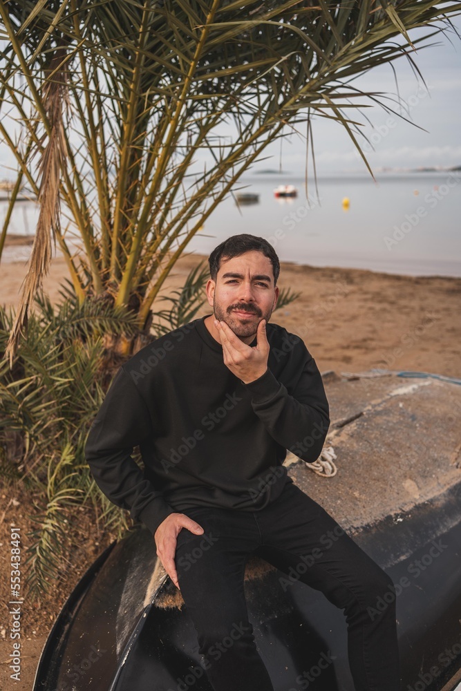 Caucasian man wearing black clothing on a beach sittin on a black boat in winter Stock 写真