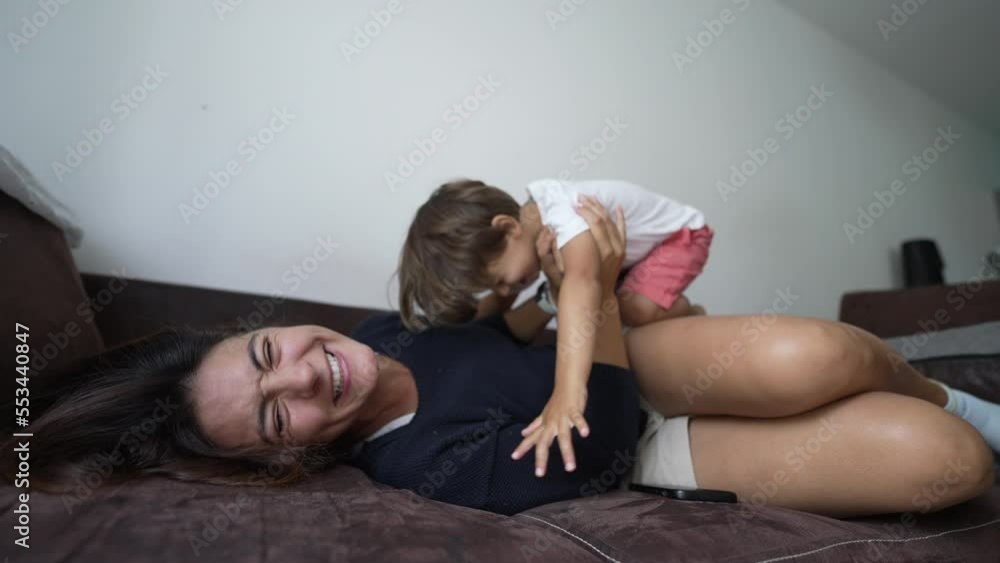Son jumping on mother lying on couch at home. Happy child diving into parent. Lifestyle joyful moment Son jumping on mother lying on couch at home. Happy child diving into parent. Lifestyle joyful moment