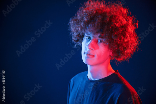 Portrait of young man with curly hair that is standing indoors, illuminated by neon lighting