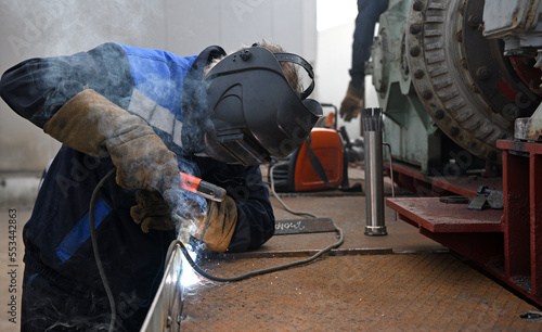 A worker welding metal parts on a construction site. A welder welds parts of a large machine in a metallurgical workshop.. An interesting example of manual work.