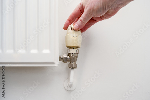 close up of plumber person turning up a thermostatically controlled radiator valve. photo