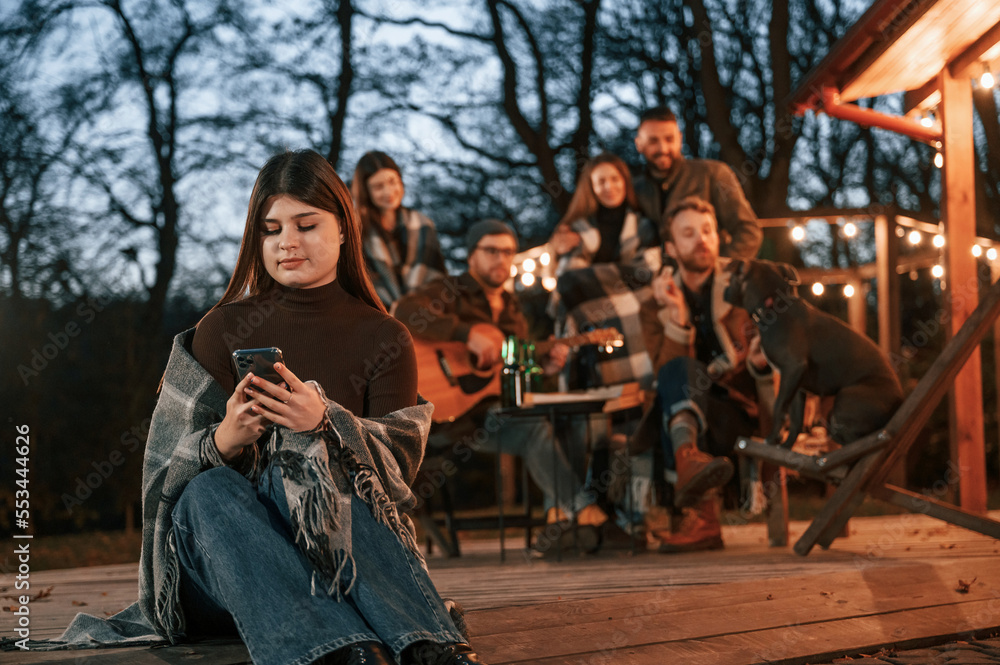 Beautiful young woman is sitting. Group of people is spending time together on the backyard at evening time Beautiful young woman is sitting. Group of people is spending time together on the backyard at evening time