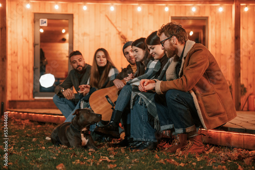 Autumn season. With dog. Group of people is spending time together on the backyard at evening time