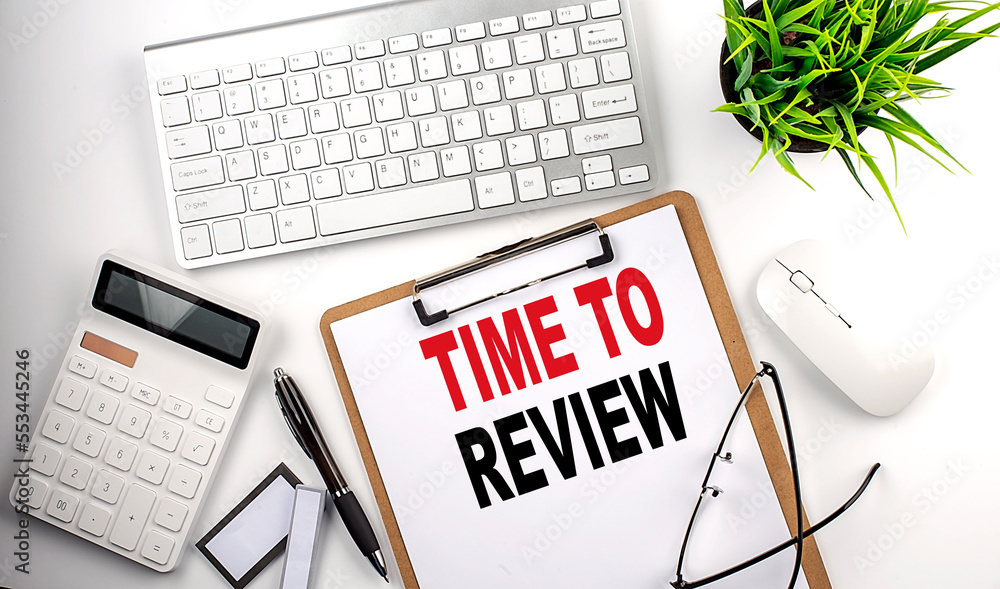Business concept.Text TIME TO REVIEW on paper clipboard with,pencil,glasses, keyboard and calculator on white background. Business concept.Text TIME TO REVIEW on paper clipboard with,pencil,glasses, keyboard and calculator on white background.