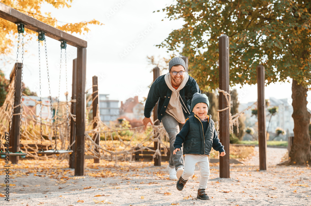 Fototapeta premium Running, having fun. Father and young son is together outdoors at daytime