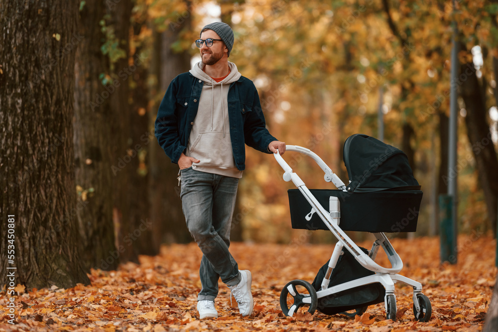 Obraz premium Front view. Man with pram is having a walk in the autumn park