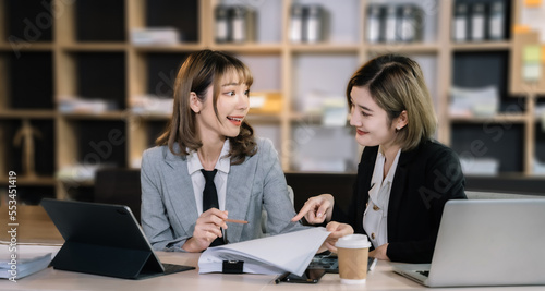 Business, technology and office concept - two business women with laptop, tablet pc computer and papers having discussion in modern office.