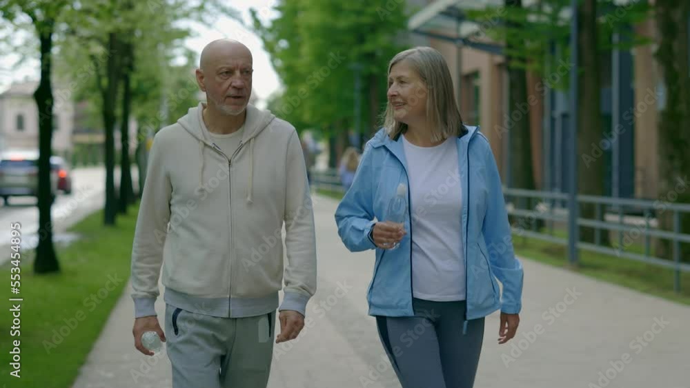 Matured sporty couple is walking after running holding the bottle of water. Sport and communication concept. Aging Youthfully Matured sporty couple is walking after running holding the bottle of water. Sport and communication concept. Aging Youthfully