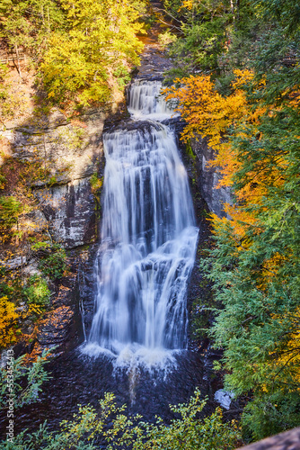 Vertical close of large waterfall from above surrounded by cliffs and fall forests