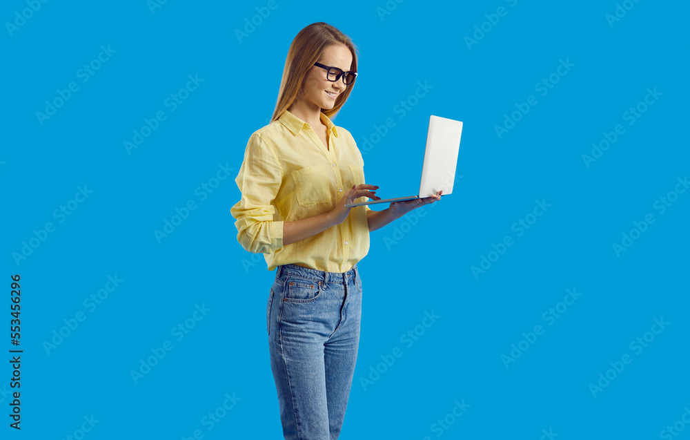 Happy young woman worker or employee work on laptop isolated on blue studio background. Smiling millennial student use computer study on internet. Remote job and technology. Happy young woman worker or employee work on laptop isolated on blue studio background. Smiling millennial student use computer study on internet. Remote job and technology.