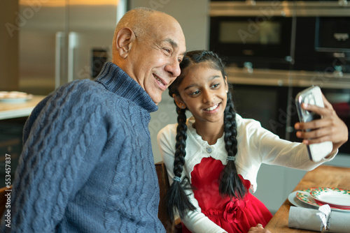 Smiling girl with grandfather taking selfie at table