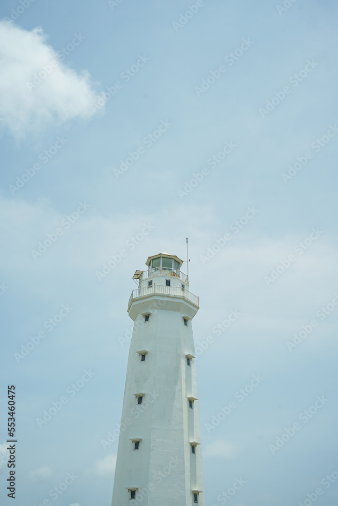 A lighthouse on the beach painted white against a blue sky background