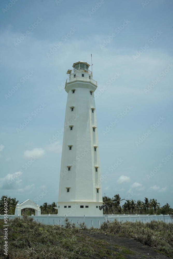 A lighthouse on the beach painted white against a blue sky background
