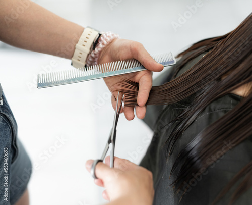 Hairdresser hands with scissors make hair cut in a beauty salon. Girl during beauty routine in barbershop