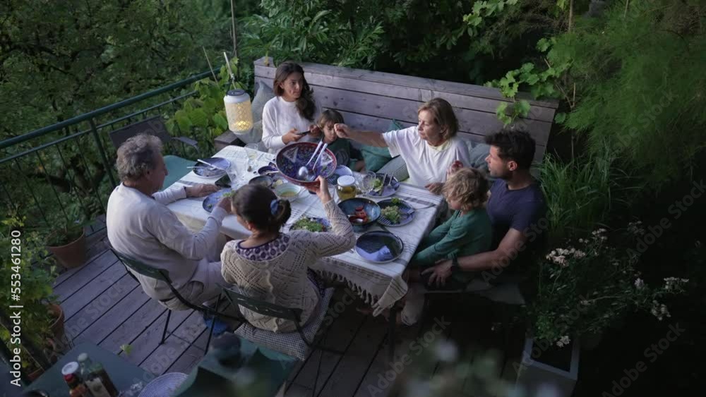 Family eating dinner together at home patio. Above view of grandparents parents and children enjoying time together over meal at dusk time. Candid and authentic Family eating dinner together at home patio. Above view of grandparents parents and children enjoying time together over meal at dusk time. Candid and authentic