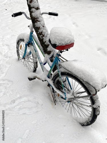 Велосипед оставленный у дерева на улице после снегопада