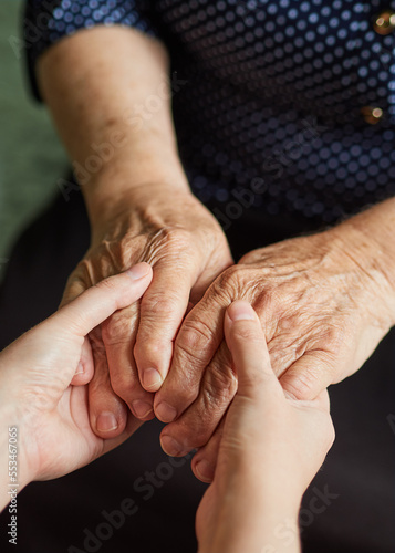 Hands of a young and old woman are holding together on a dark background