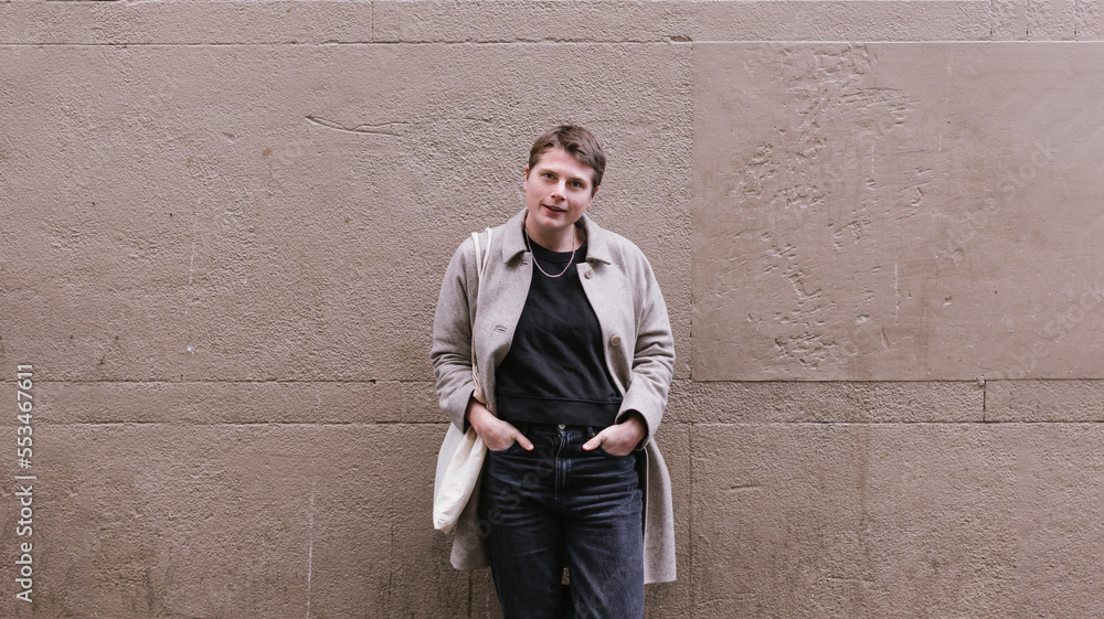 portrait of fashionable female gender fluid person standing against wall portrait of fashionable female gender fluid person standing against wall
