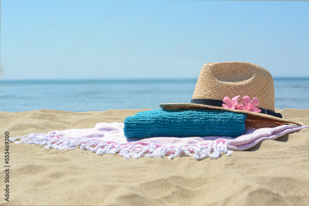 Blanket with towel, stylish straw hat and flowers on sand near sea, space for text. Beach accessories Blanket with towel, stylish straw hat and flowers on sand near sea, space for text. Beach accessories