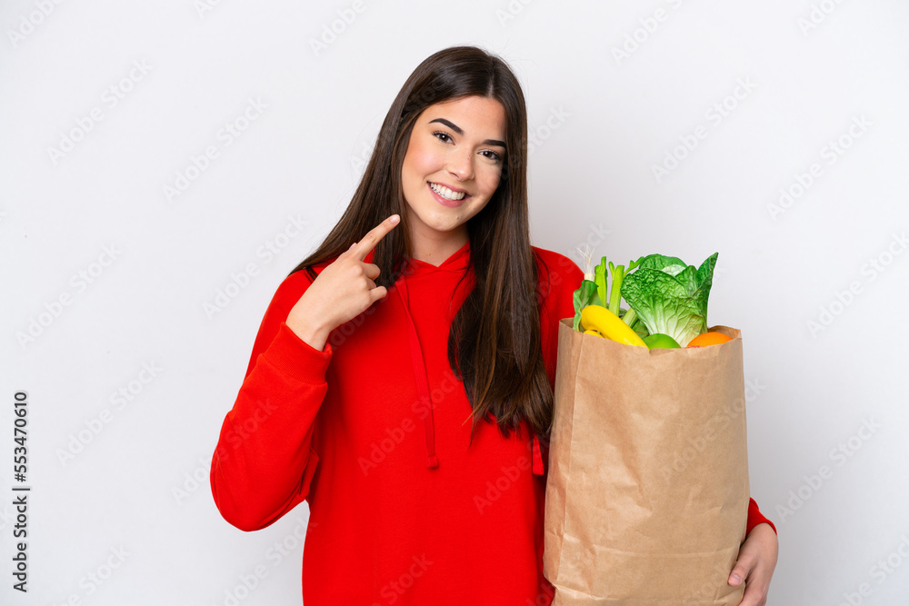Young Brazilian woman holding a grocery shopping bag isolated on white background giving a thumbs up gesture Young Brazilian woman holding a grocery shopping bag isolated on white background giving a thumbs up gesture