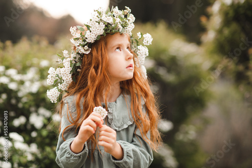 Cute child girl 4-5 year old wear floral wreath and vintage dress over flower background close up. Springtime.