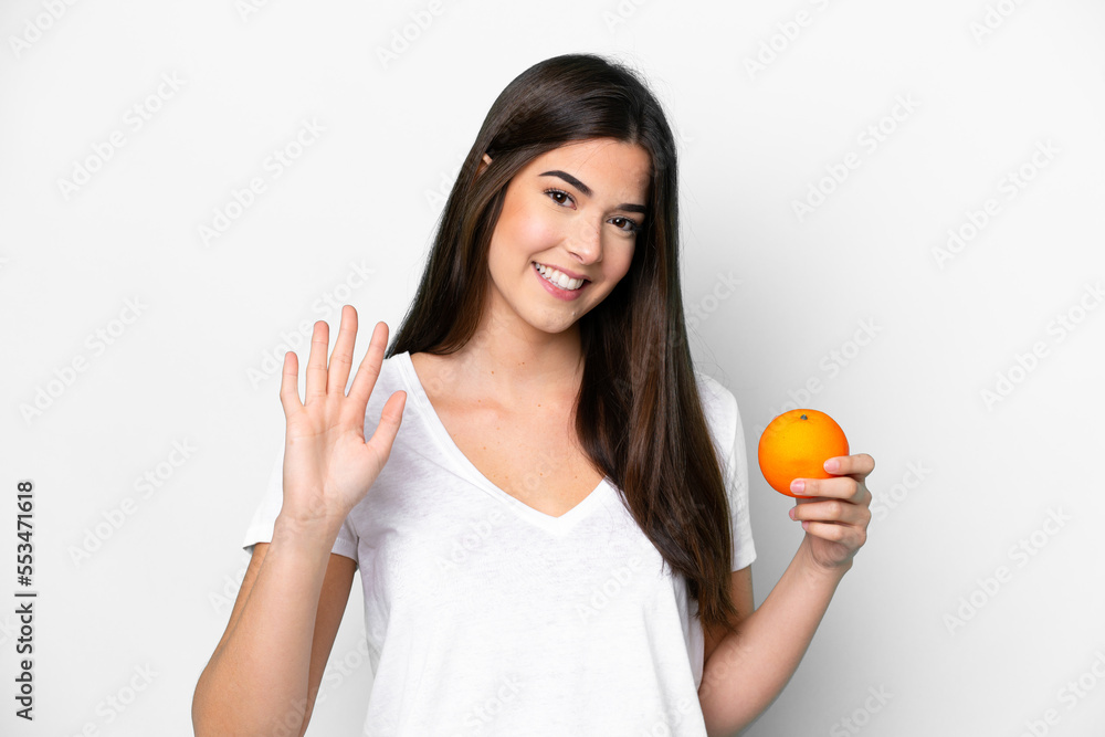Young Brazilian woman holding an orange isolated on white background saluting with hand with happy expression Young Brazilian woman holding an orange isolated on white background saluting with hand with happy expression