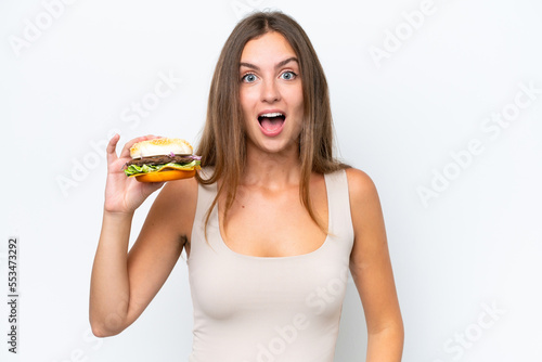Young pretty woman holding a burger isolated on white background with surprise and shocked facial expression