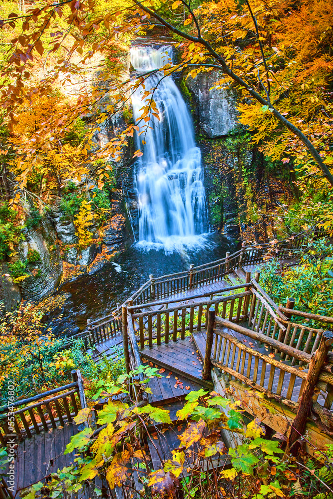 Obraz premium Boardwalk stairs lead down to stunning large waterfall over cliffs surrounded by yellow fall foliage
