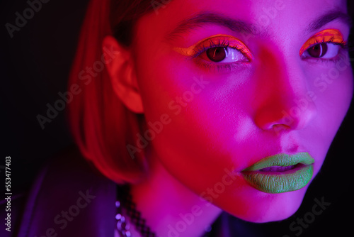 close up portrait of woman with glowing neon makeup in purple light on black background.