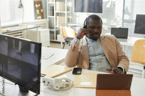 Portrait of black man speaking via headset and consulting customer in call center or tech support office
