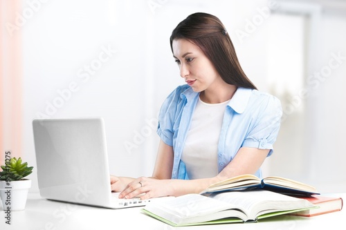 Serious young student studying with books and laptop