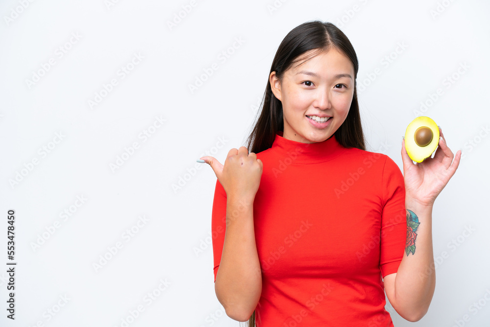 Young Asian woman holding an avocado isolated on white background pointing to the side to present a product Young Asian woman holding an avocado isolated on white background pointing to the side to present a product