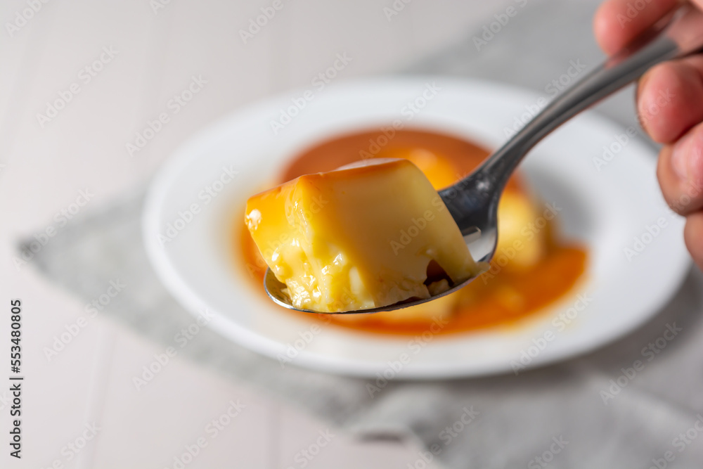 pudim de leite, also known as flan or milk pudding, isolated on white table  with grey cloth. bitten slice with a metallic spoon concept of traditional  brazilian dessert Photos