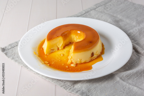 pudim de leite, also known as flan or milk pudding, isolated on white table with grey cloth. bitten slice with a metallic spoon concept of traditional brazilian dessert photo