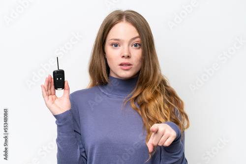 Young caucasian woman holding car keys isolated on white background surprised and pointing front