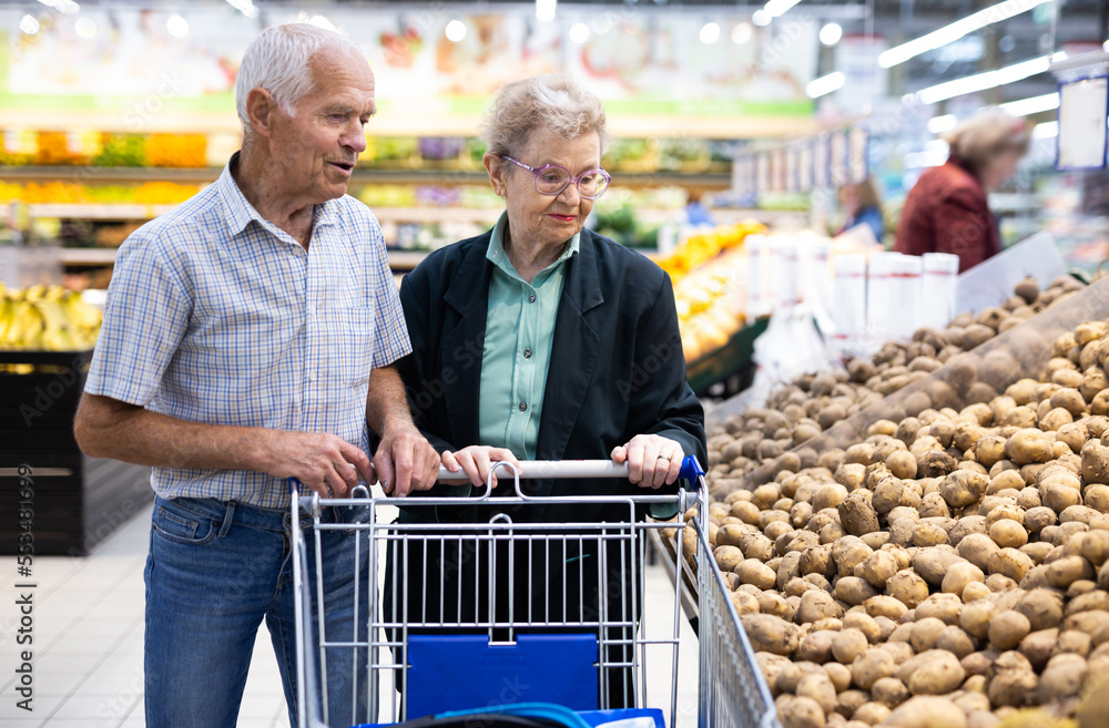 mature spouses chooses potato in vegetable section of supermarket
