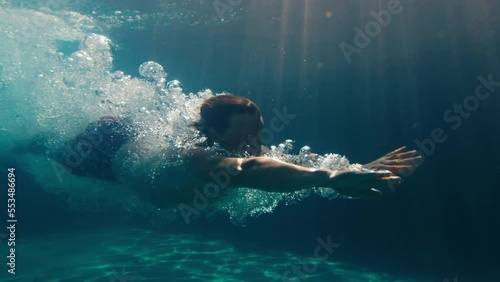 Man dives in the pool. Underwater view of the person diving in the pool and gliding underwater with bubbles