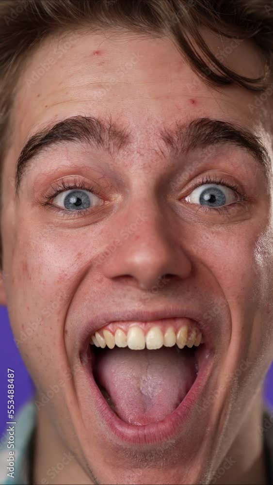 Vertical video closeup slow motion of excited jubilant overjoyed young man 20s doing winner gesture celebrate clenching fists say yes isolated on purple background studio portrait Vertical video closeup slow motion of excited jubilant overjoyed young man 20s doing winner gesture celebrate clenching fists say yes isolated on purple background studio portrait