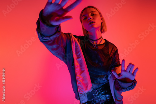 trendy woman in neon light posing with outstretched hands on coral red background.