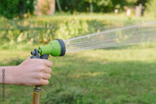 Gardeners hand holds a hose with a sprayer and watered the lawn in country house