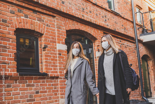 Young pretty girls friends in medical masks having fun outdoor in autumn evening in city laughing - end of pandemic concept
