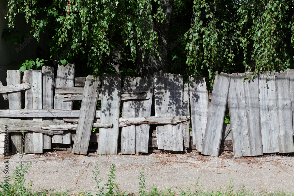 Old crooked wooden fence. Funny crooked fence in the shade of birch trees looks like a haunted house. Design element