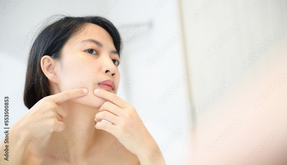 Problem skin. Concerned young asian women popping pimple on cheek while standing near mirror in bathroom. young asian women with acne Problem skin. Concerned young asian women popping pimple on cheek while standing near mirror in bathroom. young asian women with acne