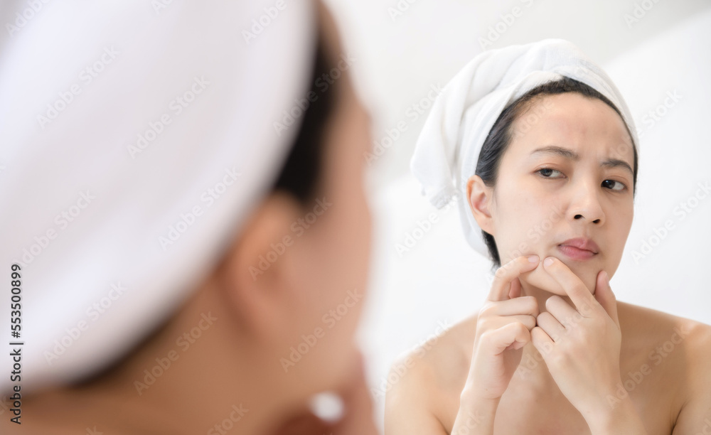 Problem skin. Concerned young asian women popping pimple on cheek while standing near mirror in bathroom. young asian women with acne