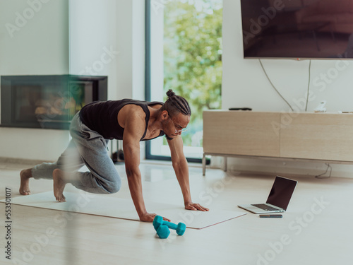 Training At Home. Sporty man doing training while watching online tutorial on laptop, exercising in living room, free space
