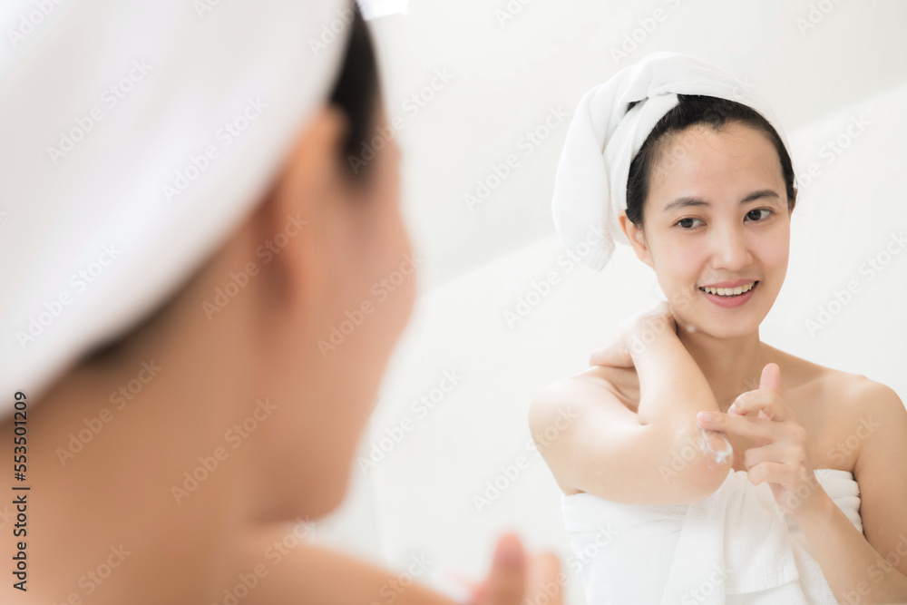 Happy young Asian woman applying lotions on her body in bathroom Happy young Asian woman applying lotions on her body in bathroom